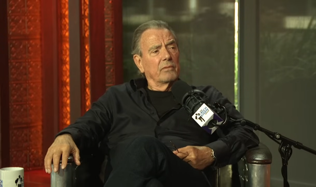 Eric Braeden in black clothes sitting in the chair near the microphone and looking at the side