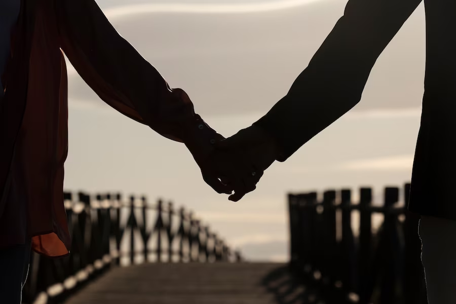 Silhouetted couple holding hands while walking on a bridge