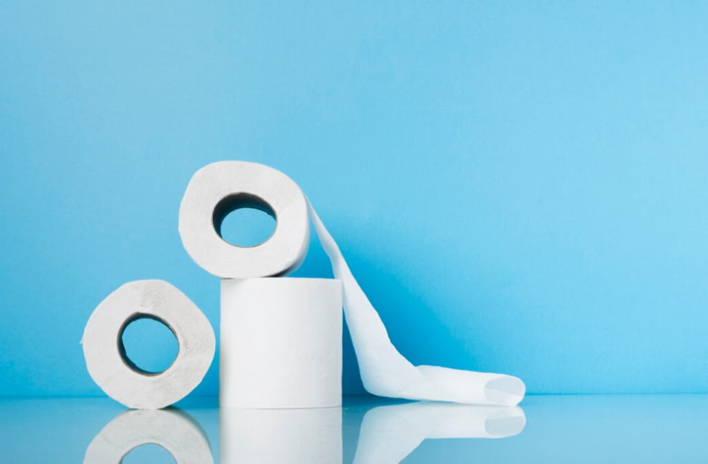Three rolls of white toilet paper against a bright blue background, reflecting on a shiny surface below