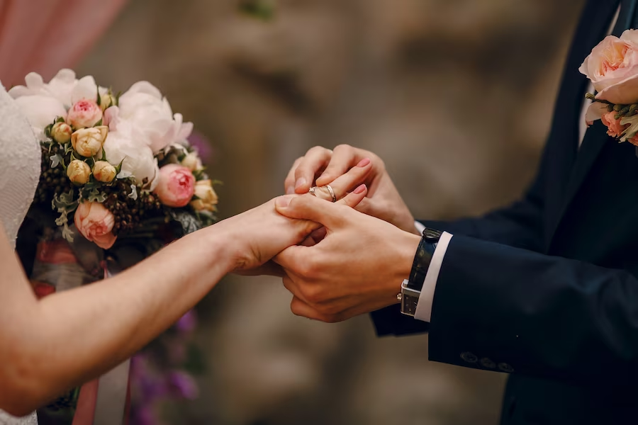 Close-up photo of a hand during a wedding, with the groom placing a ring on the bride